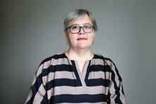 GPT Icon  Foto: Person mit grauem Haar und Brille vor neutralem Hintergrund, trägt ein gestreiftes Oberteil.